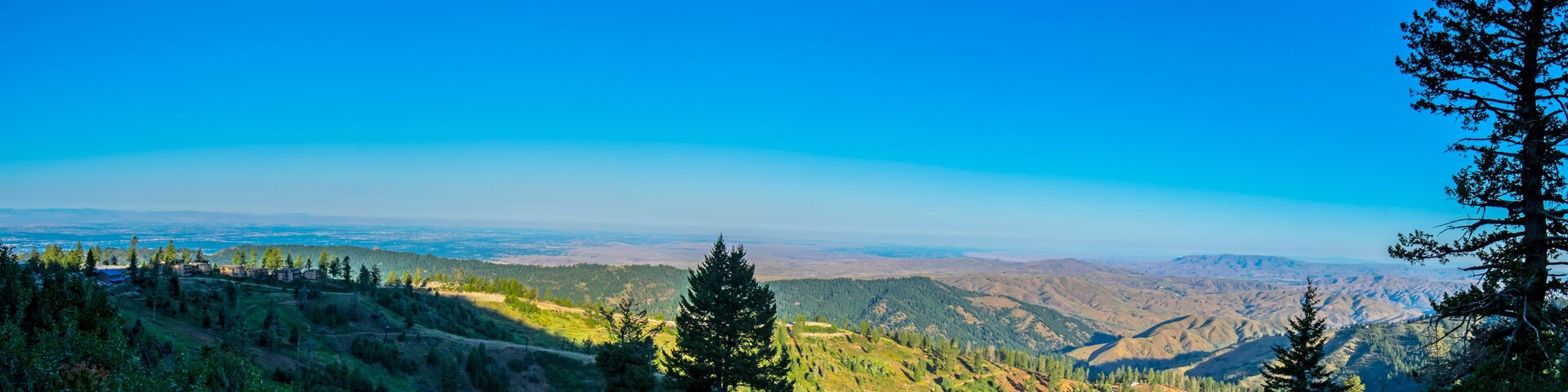 A mountainous landscape with dense forests, a clear blue sky, and distant hills.