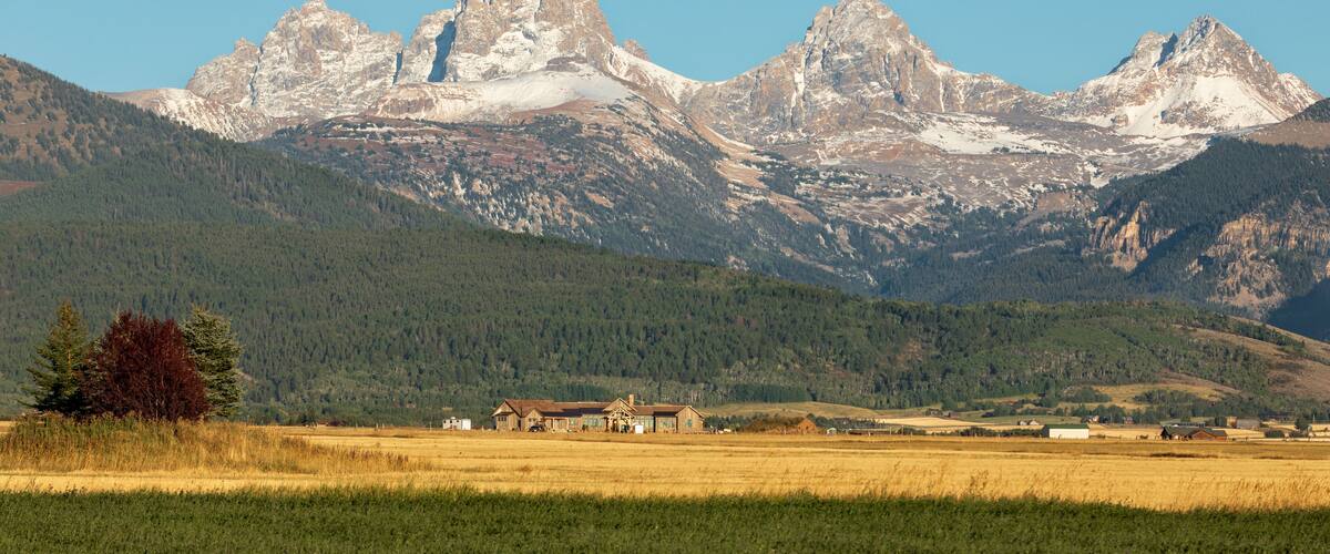 A mountain range with a prominent peak, a small settlement with buildings, and a field in the foreground.