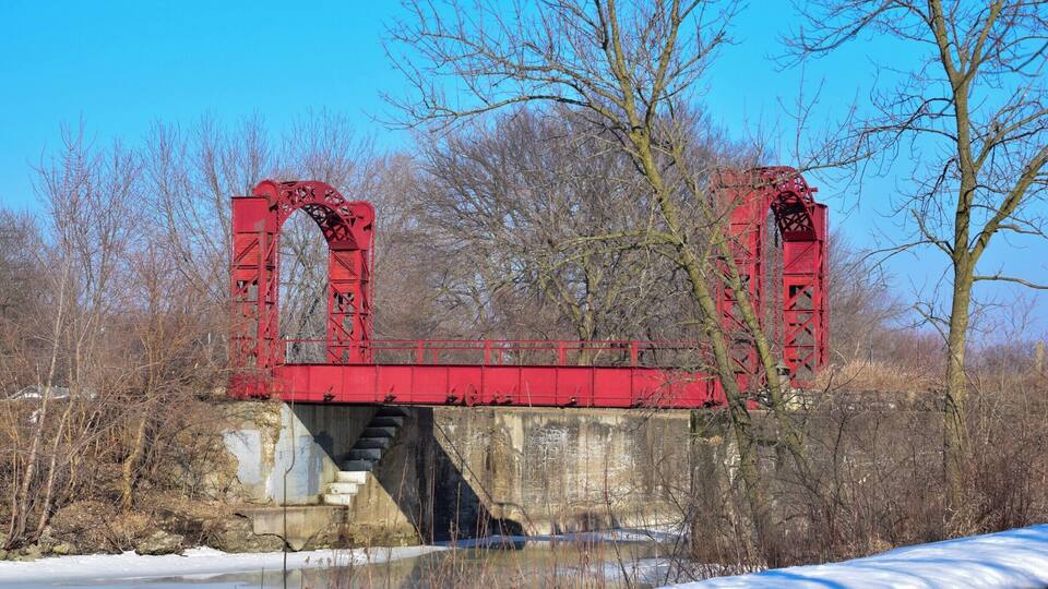 A red metal bridge over a river with snow on the ground.