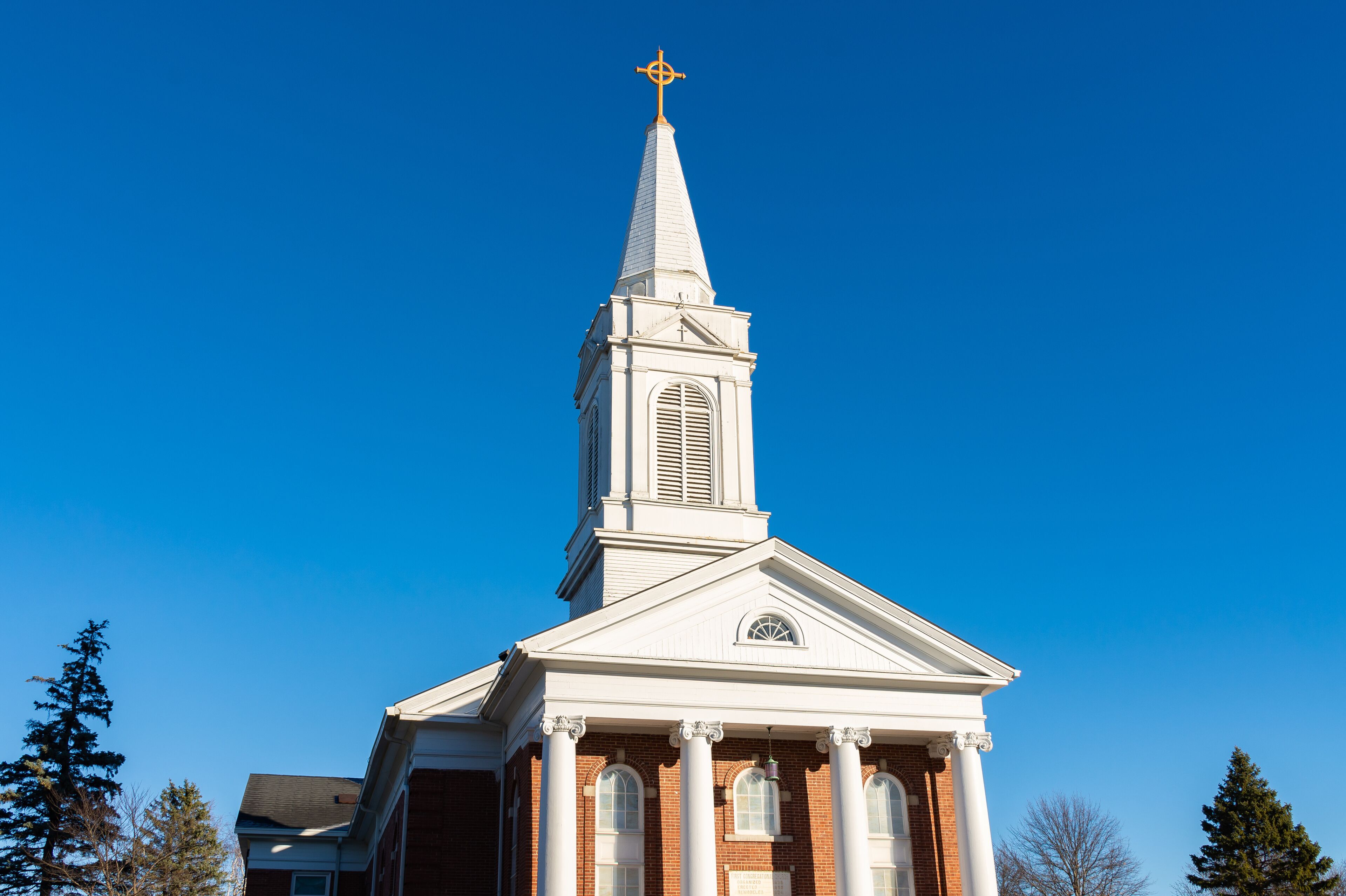 A church with a white steeple and a cross at the top.