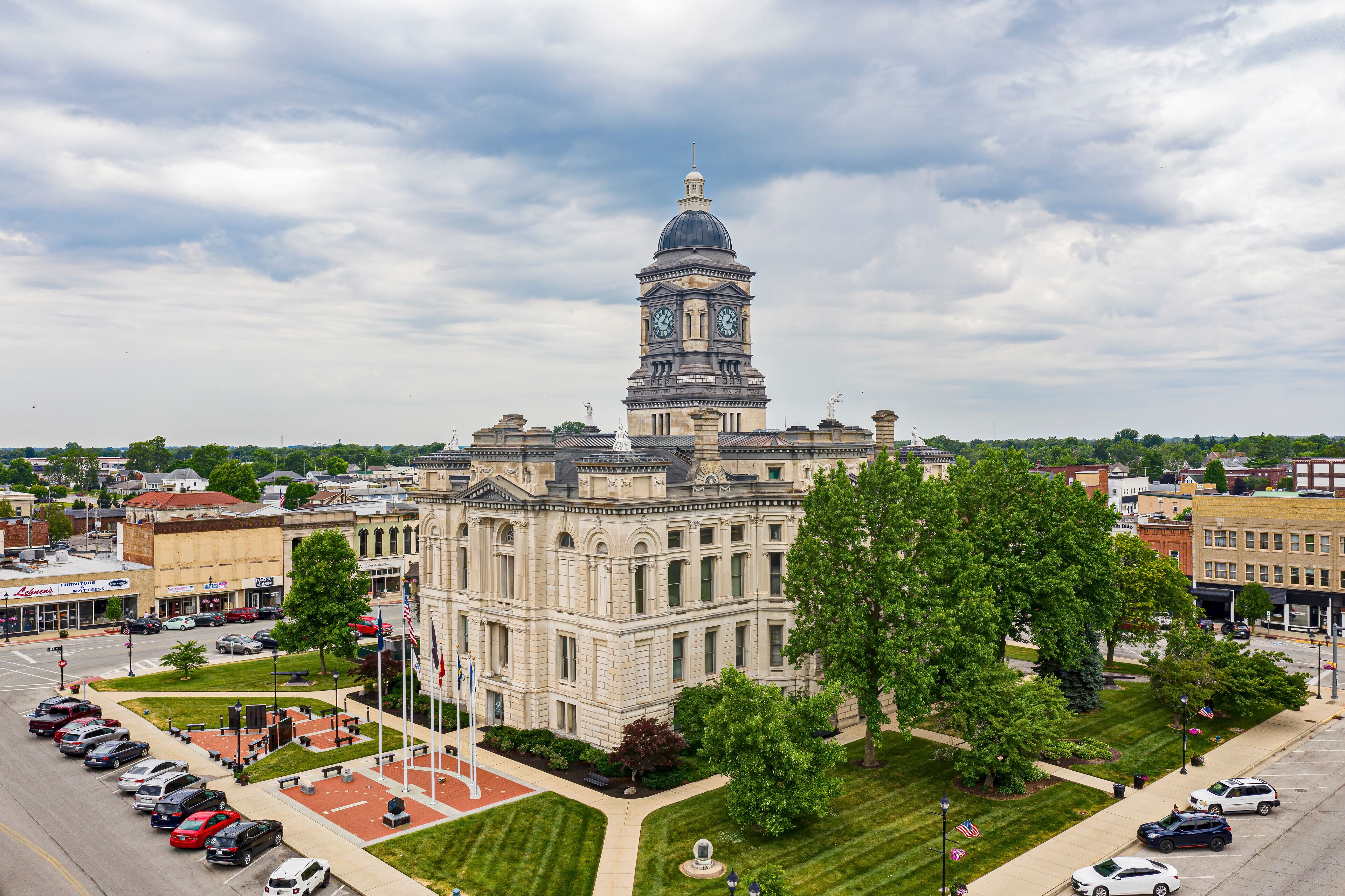 A historic building with a clock tower, surrounded by a parking lot and greenery.