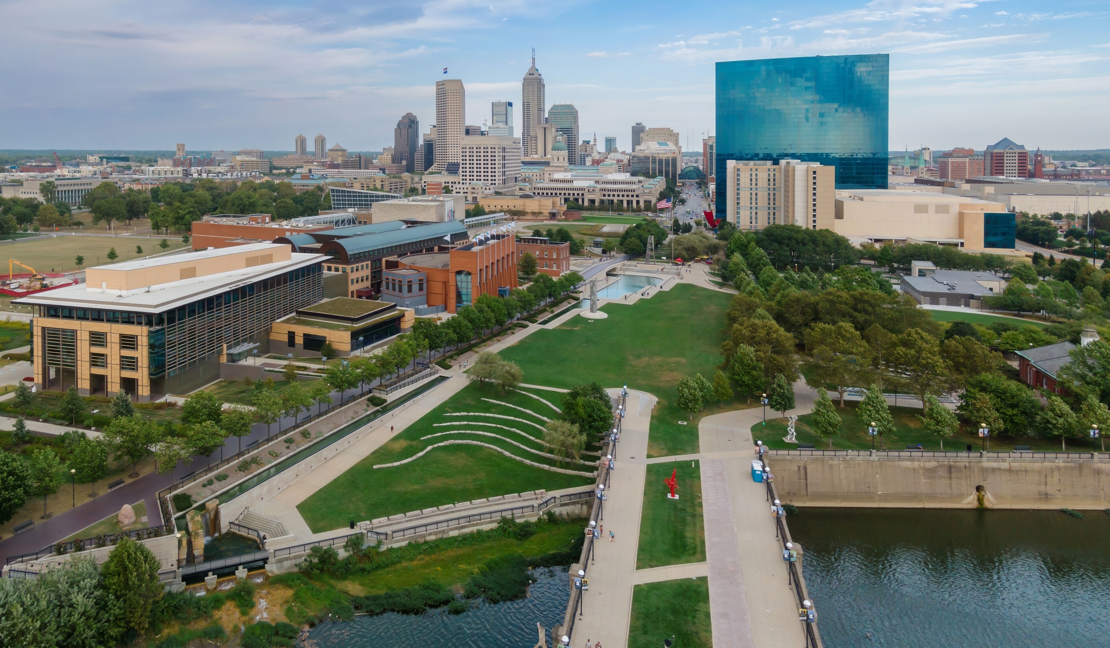 An aerial view of a city with a river, green spaces, and various buildings including a large modern glass building.