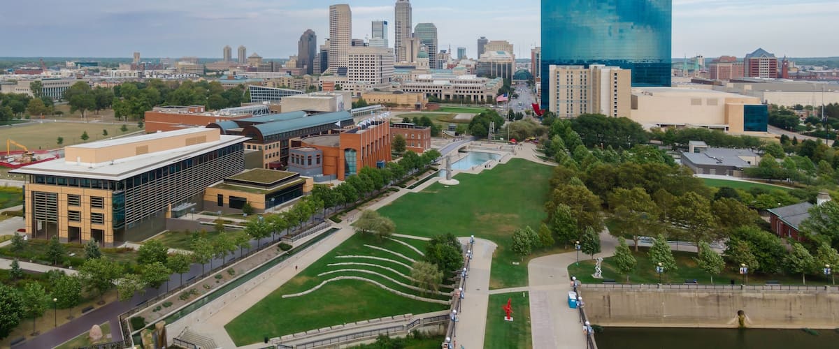 An aerial view of a city with a river, green spaces, and various buildings including a large modern glass building.