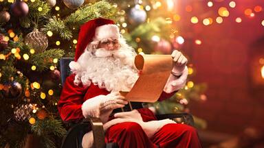 Santa Claus Sitting at His Room at Home Near Christmas Tree and Reading Christmas Letter or Wish List