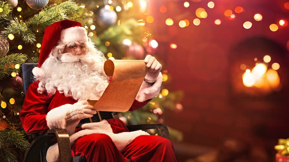 Santa Claus Sitting at His Room at Home Near Christmas Tree and Reading Christmas Letter or Wish List