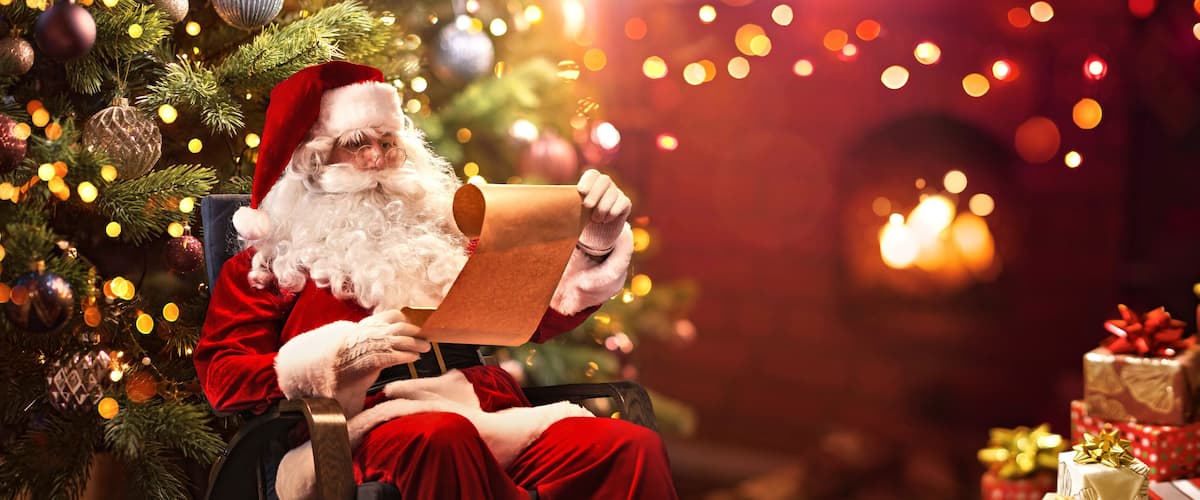 Santa Claus seated by a Christmas tree with wrapped gifts.