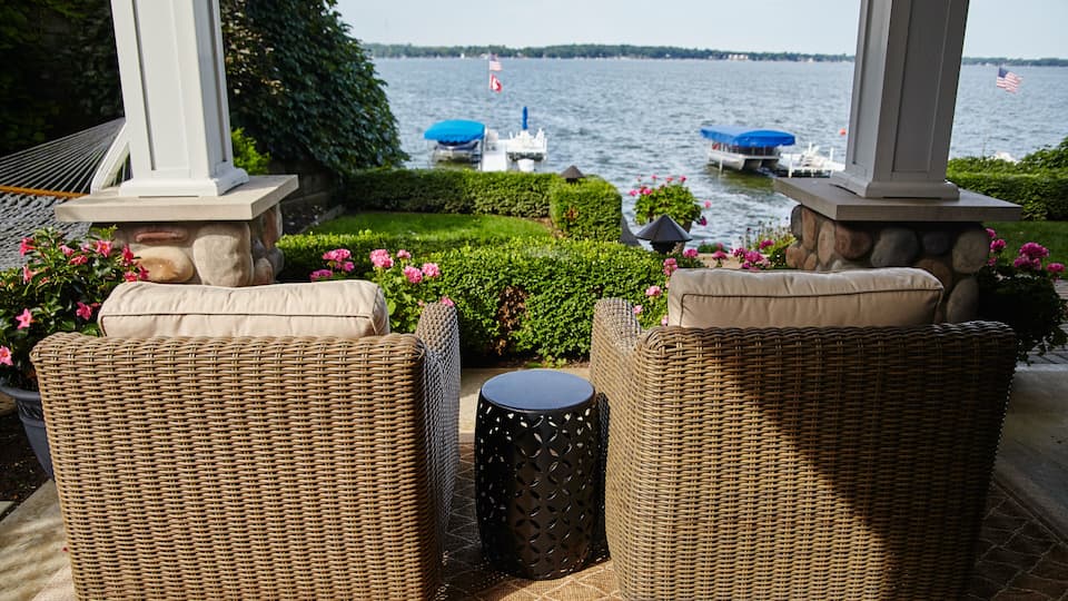 Wicker furniture, a small round table, and a view of a lake with boats.