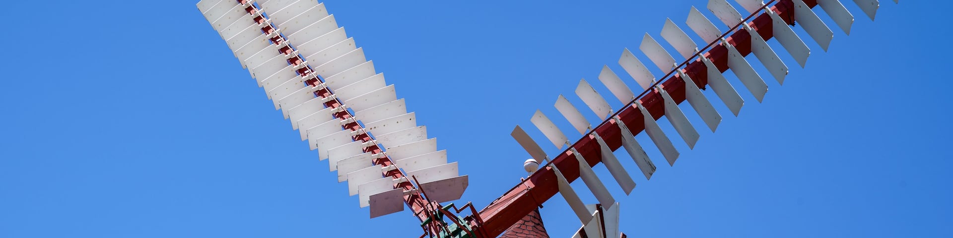 A traditional windmill with white sails and a red base, set against a clear blue sky.