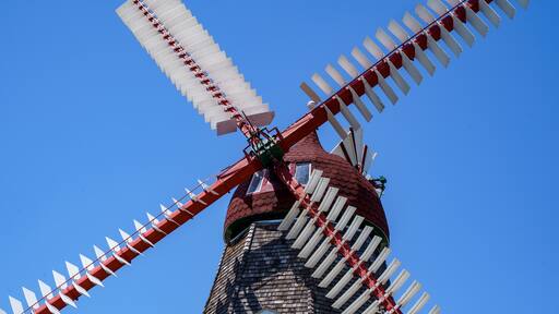 Un moulin à vent traditionnel, avec ses voiles blanches et sa base rouge, se dressant sur un ciel bleu dégagé.
