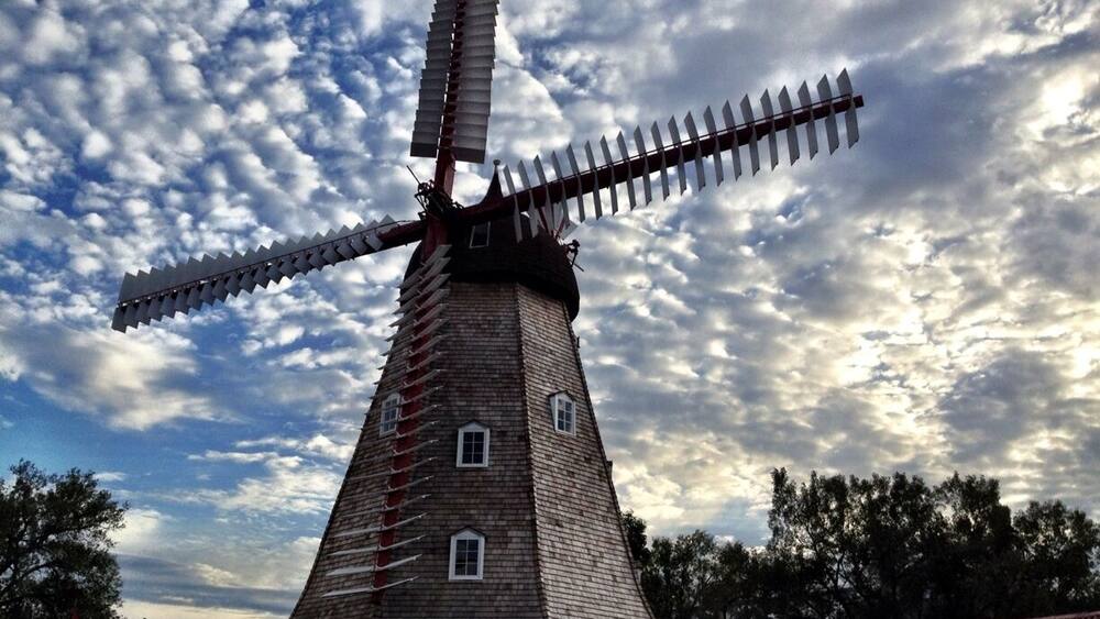 A traditional windmill with a wooden structure and a large sail, set against a cloudy sky.
