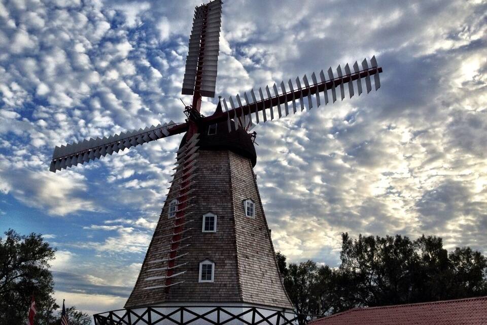 A traditional windmill with a wooden structure and a large sail, set against a cloudy sky.