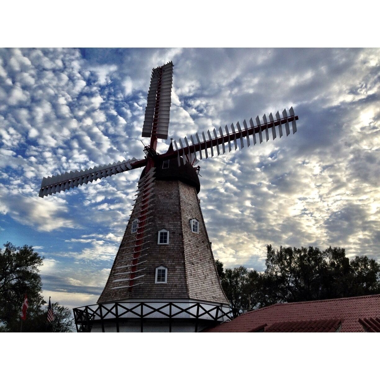A traditional windmill with a wooden structure and a large sail, set against a cloudy sky.