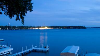 A calm lake at dusk with docked boats and a distant city skyline.