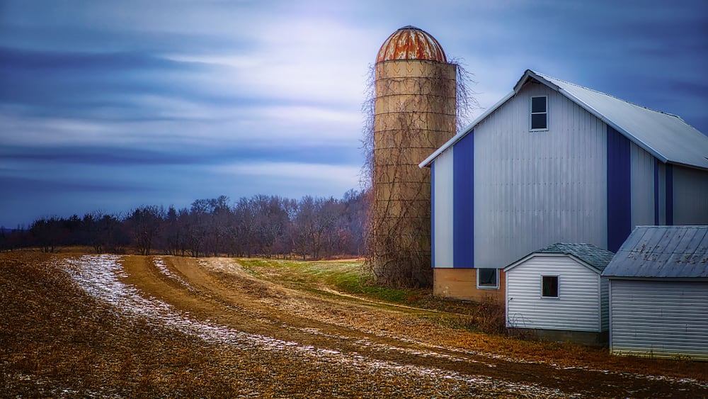 A quiet midwestern farmstead in winter, with glowing sky, silo and blue and white barn
