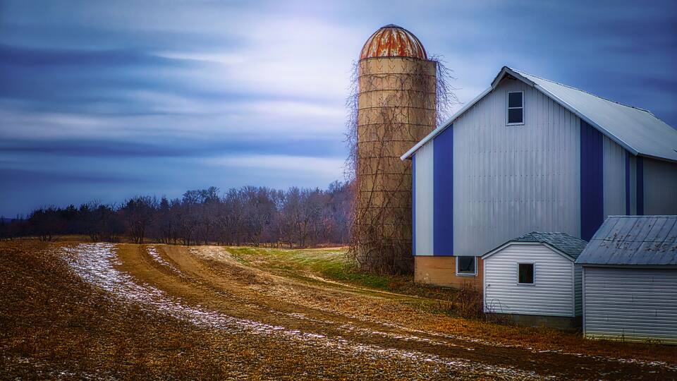 A barn, a silo, and a dirt road in a rural setting.
