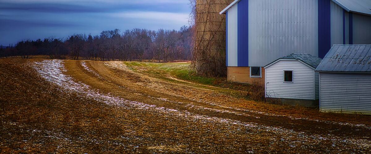 A barn, a silo, and a dirt road in a rural setting.