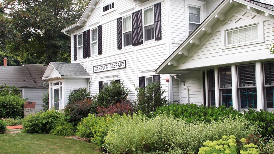 A white building with black shutters and a sign that reads "Hampton Library."
