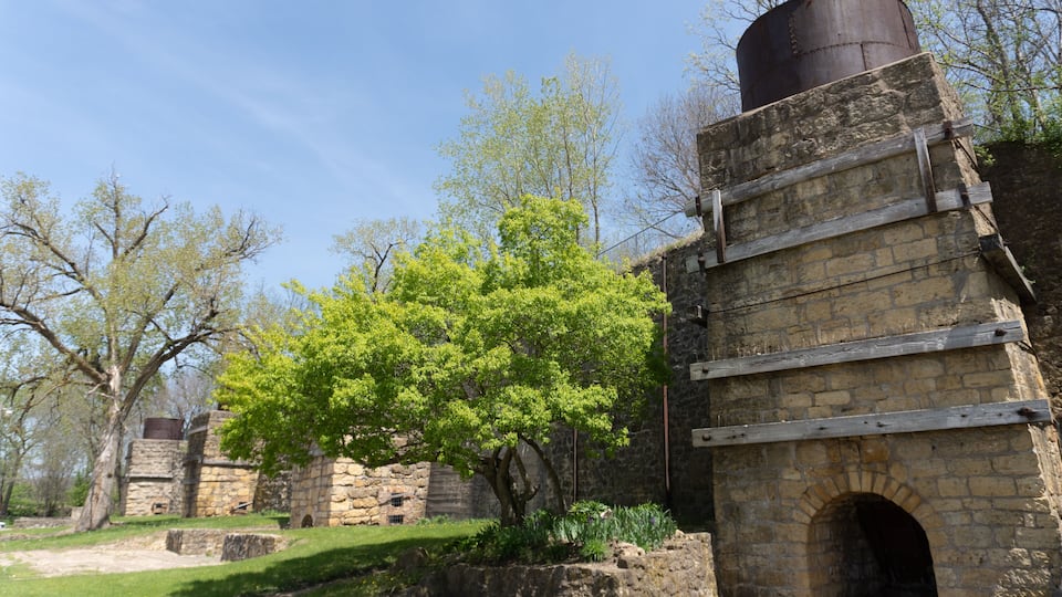 An old stone building with a large metal tank on top, surrounded by trees and a grassy area.