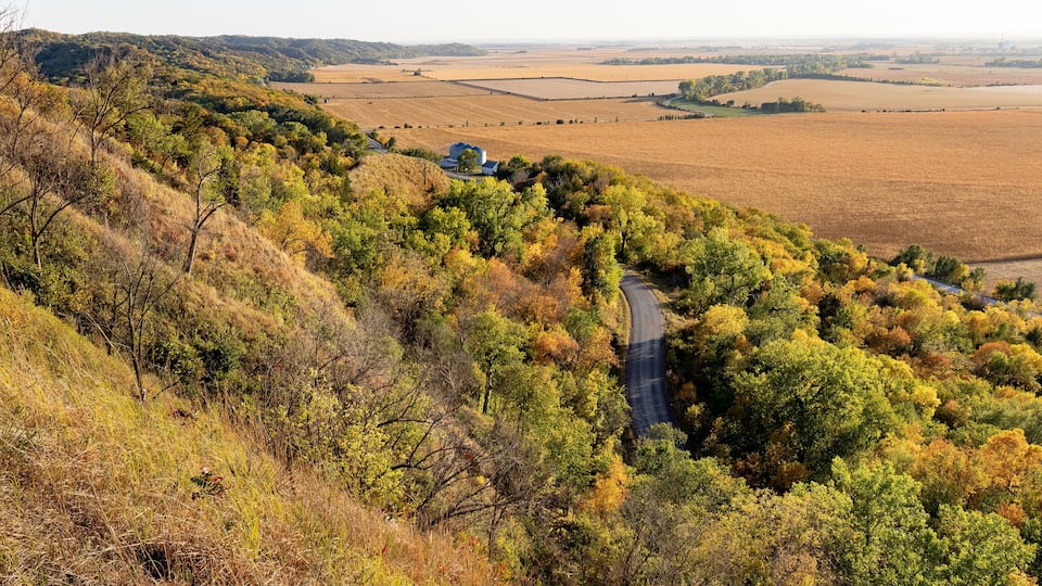 A winding road through a hilly area with autumn-colored trees and fields.