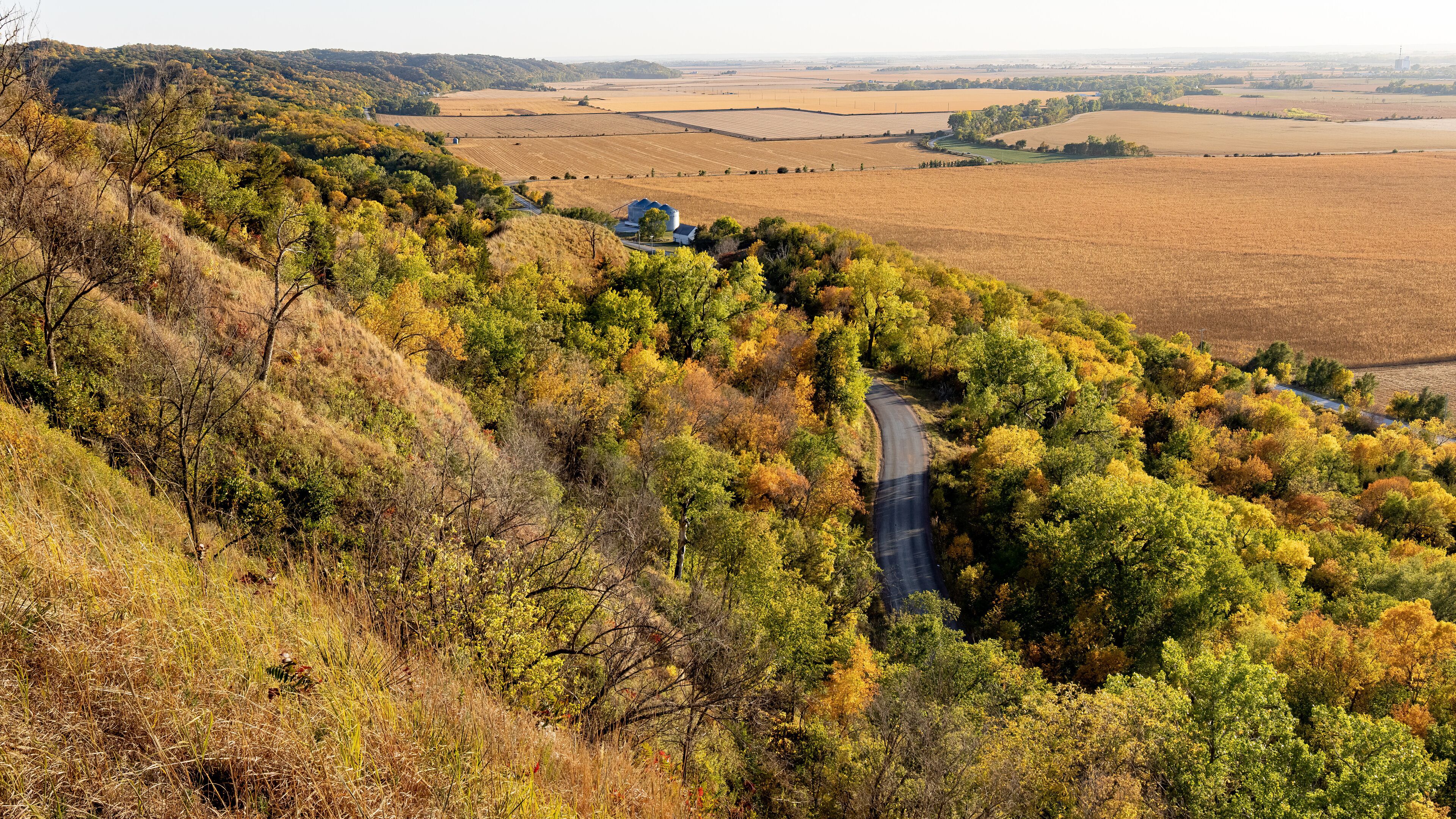 A winding road through a hilly area with autumn-colored trees and fields.