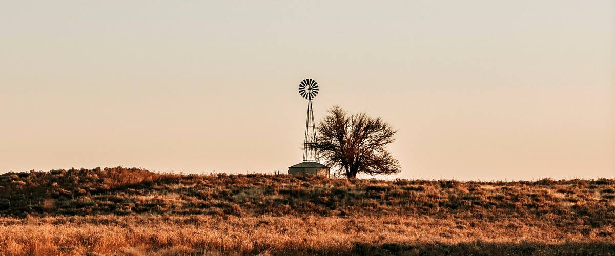 A windmill on a hill with sparse vegetation.
