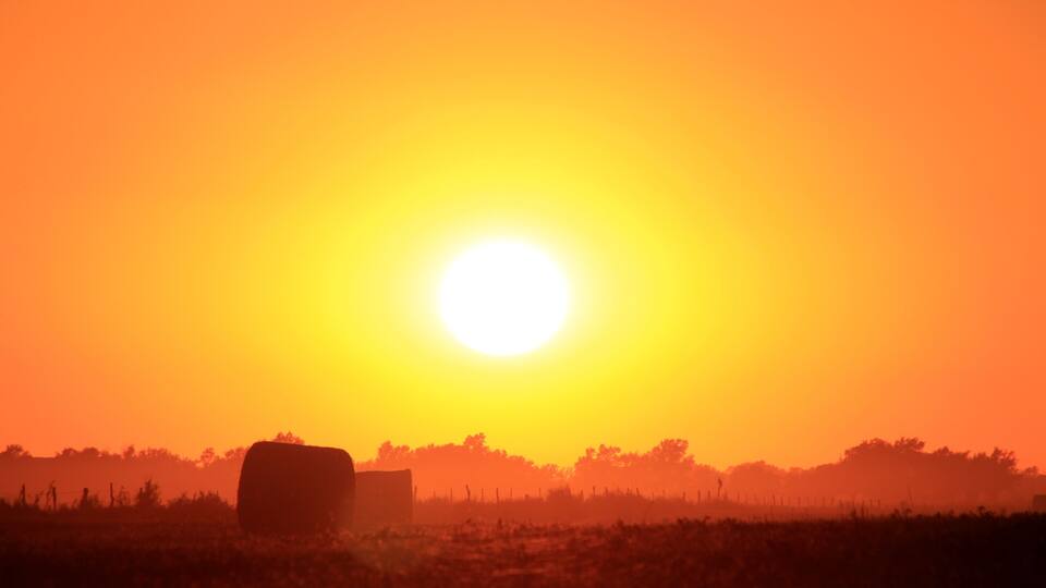 A sunset over a field with hay bales.