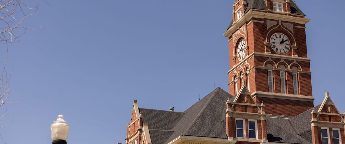 A large brick building with a clock tower and a street lamp.