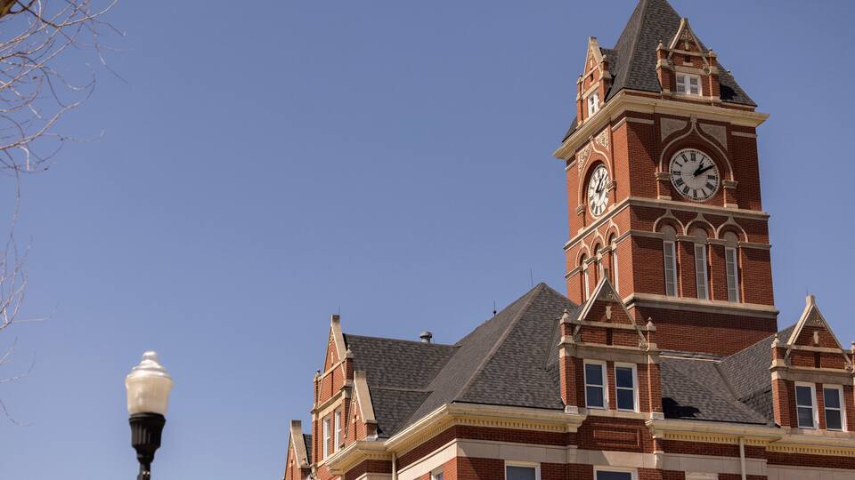 A large brick building with a clock tower and a street lamp.