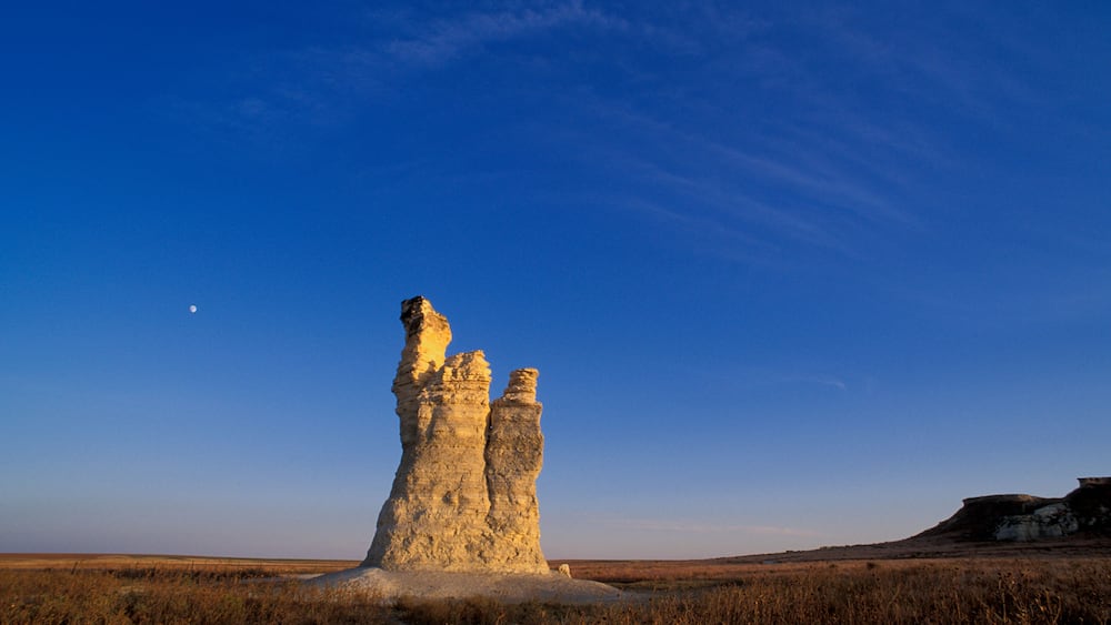 A rock formation in a flat landscape under a clear blue sky.