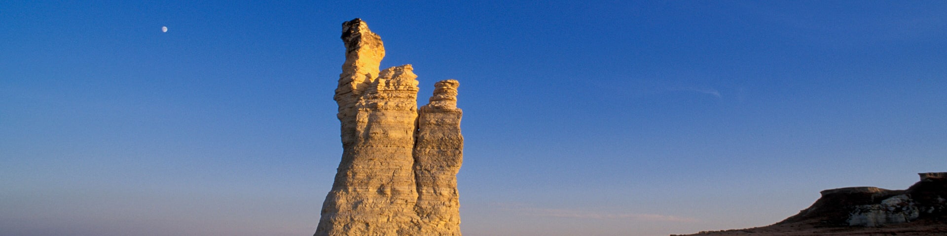 A rock formation in a flat landscape under a clear blue sky.