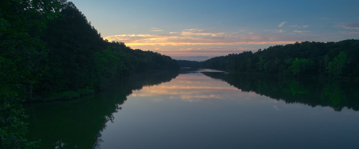 A calm river flanked by dense forests under a twilight sky.