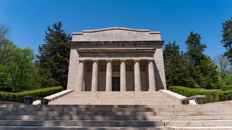 A neoclassical building with a stepped entrance, flanked by columns and surrounded by greenery.