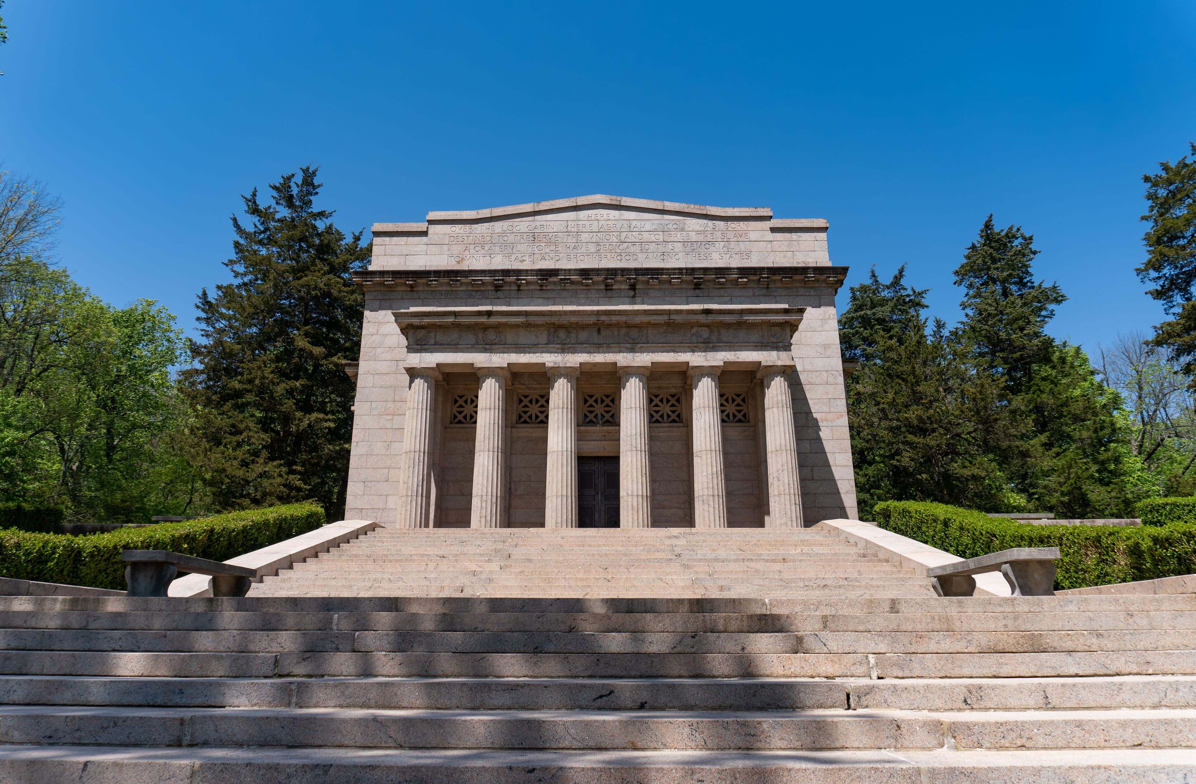 A neoclassical building with a stepped entrance, flanked by columns and surrounded by greenery.