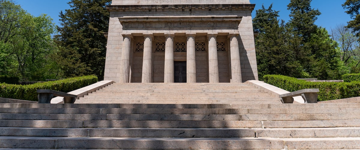A neoclassical building with a stepped entrance, flanked by columns and surrounded by greenery.