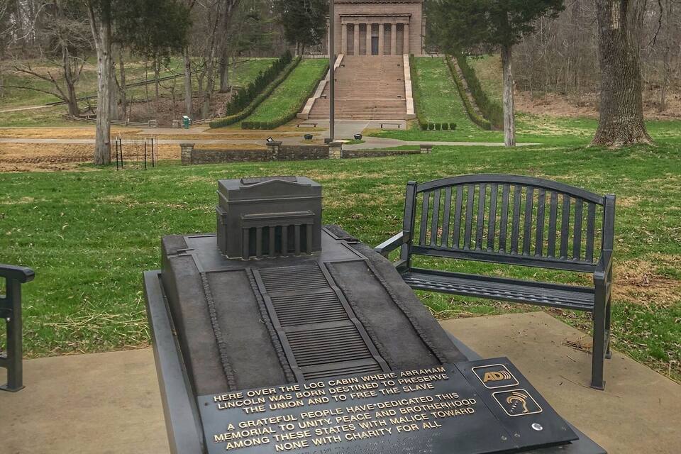 Um memorial com uma placa, um banco e um mastro com a bandeira americana.