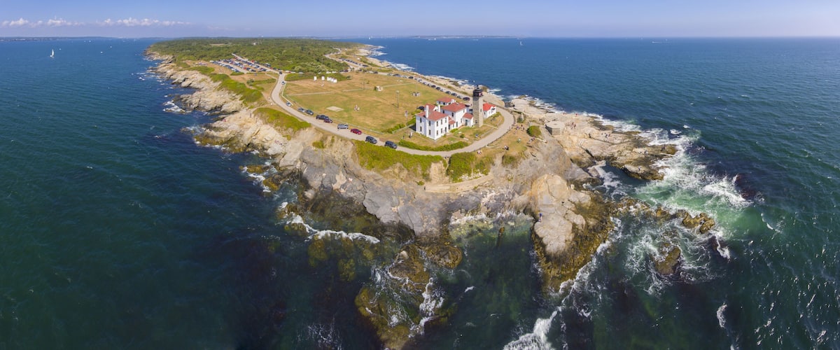 An aerial view of a coastal area with a lighthouse, a parking lot, and a rocky shoreline.