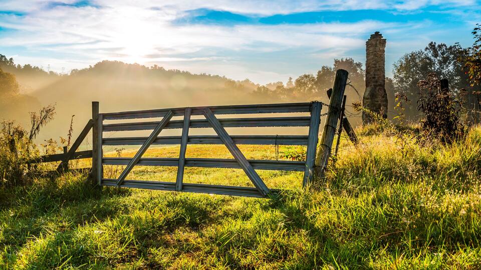 A rustic wooden gate in a grassy field with a stone tower in the background.