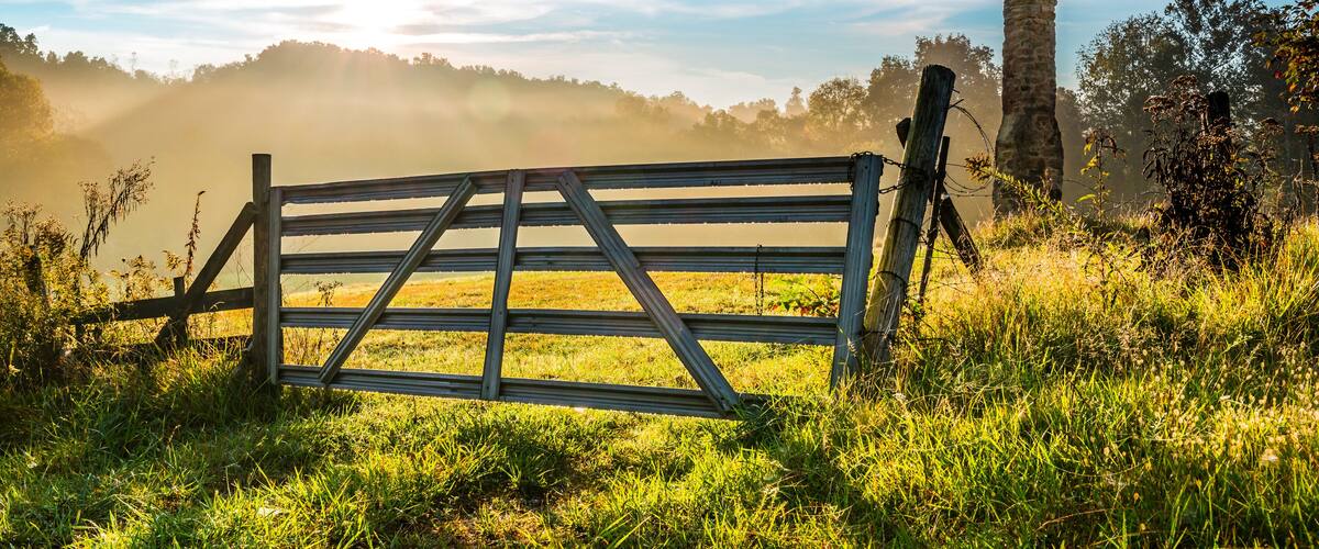 A rustic wooden gate in a grassy field with a stone tower in the background.