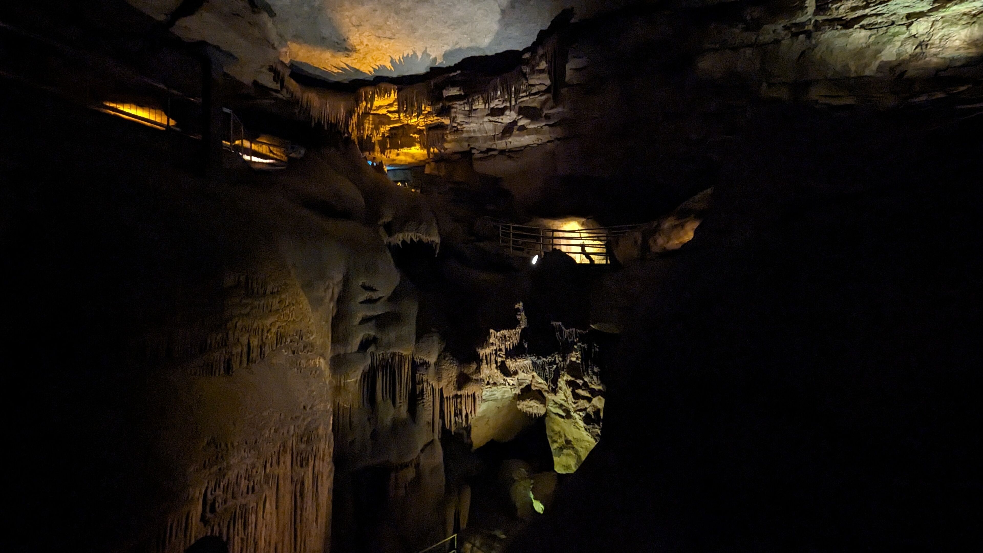 A cave with stalactites and stalagmites, illuminated by artificial lighting.