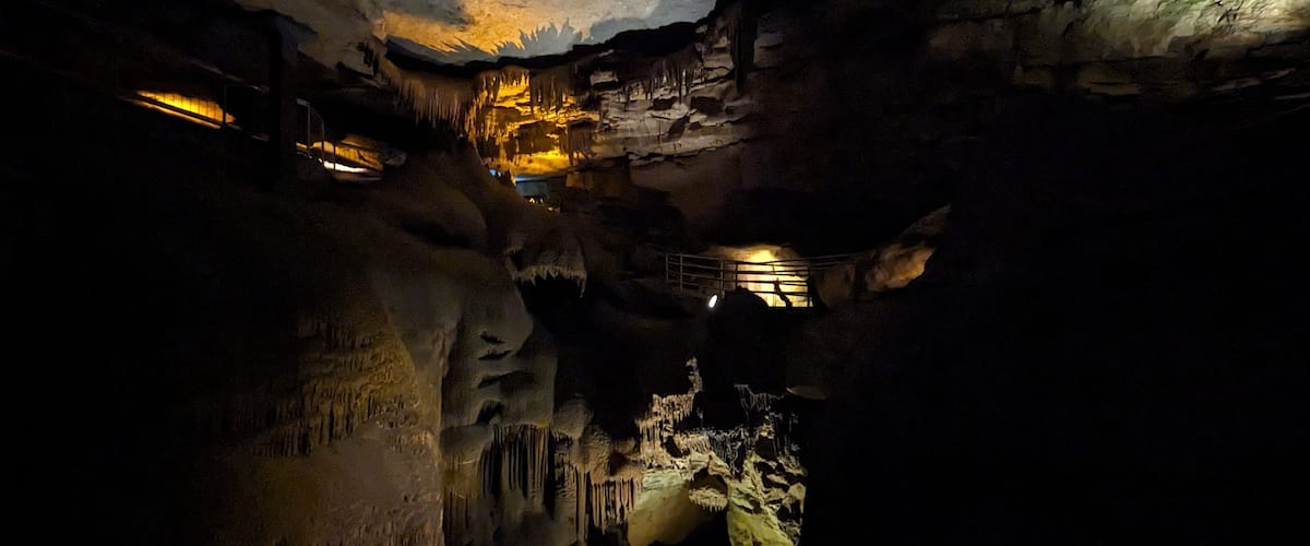 A cave with stalactites and stalagmites, illuminated by artificial lighting.