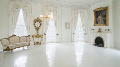 Een witte kamer met een open haard, een bank en een schilderij aan de muur.