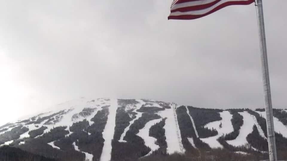 A snowy mountain with skiers, an American flag, and a sign prohibiting alcohol.