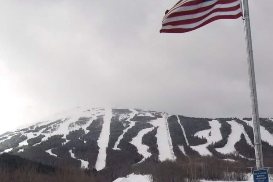 Una montagna innevata con sciatori, una bandiera americana e un cartello che vieta l'alcol.