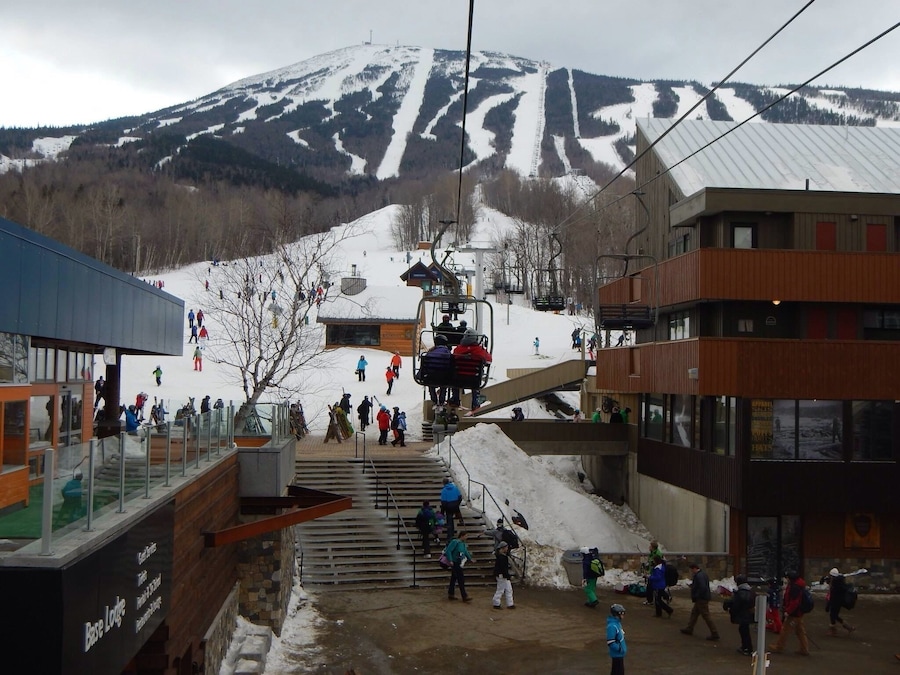 A ski lift at a mountain resort with a snowy landscape and buildings in the foreground.