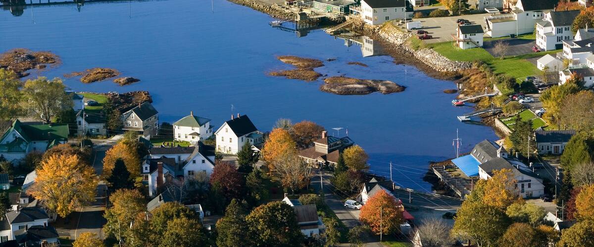 A coastal town with a pier, waterfront houses, and autumn foliage.