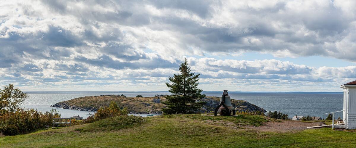 A coastal landscape with a white house, a large tree, and a rocky outcrop in the distance.