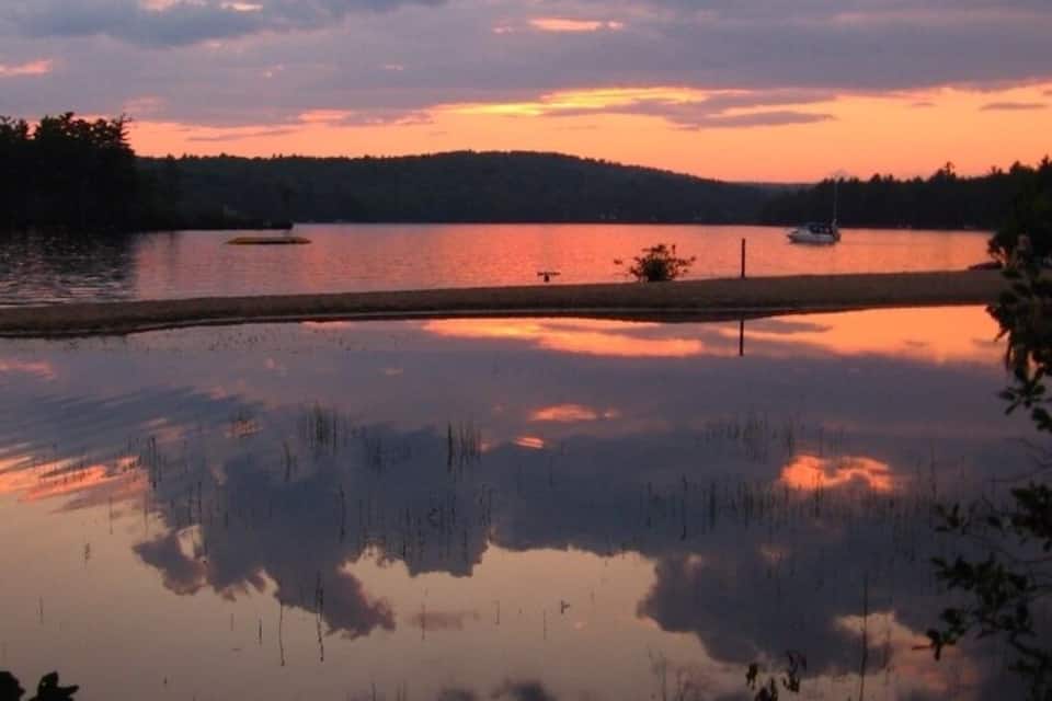 A calm lake at sunset with boats and a dock.