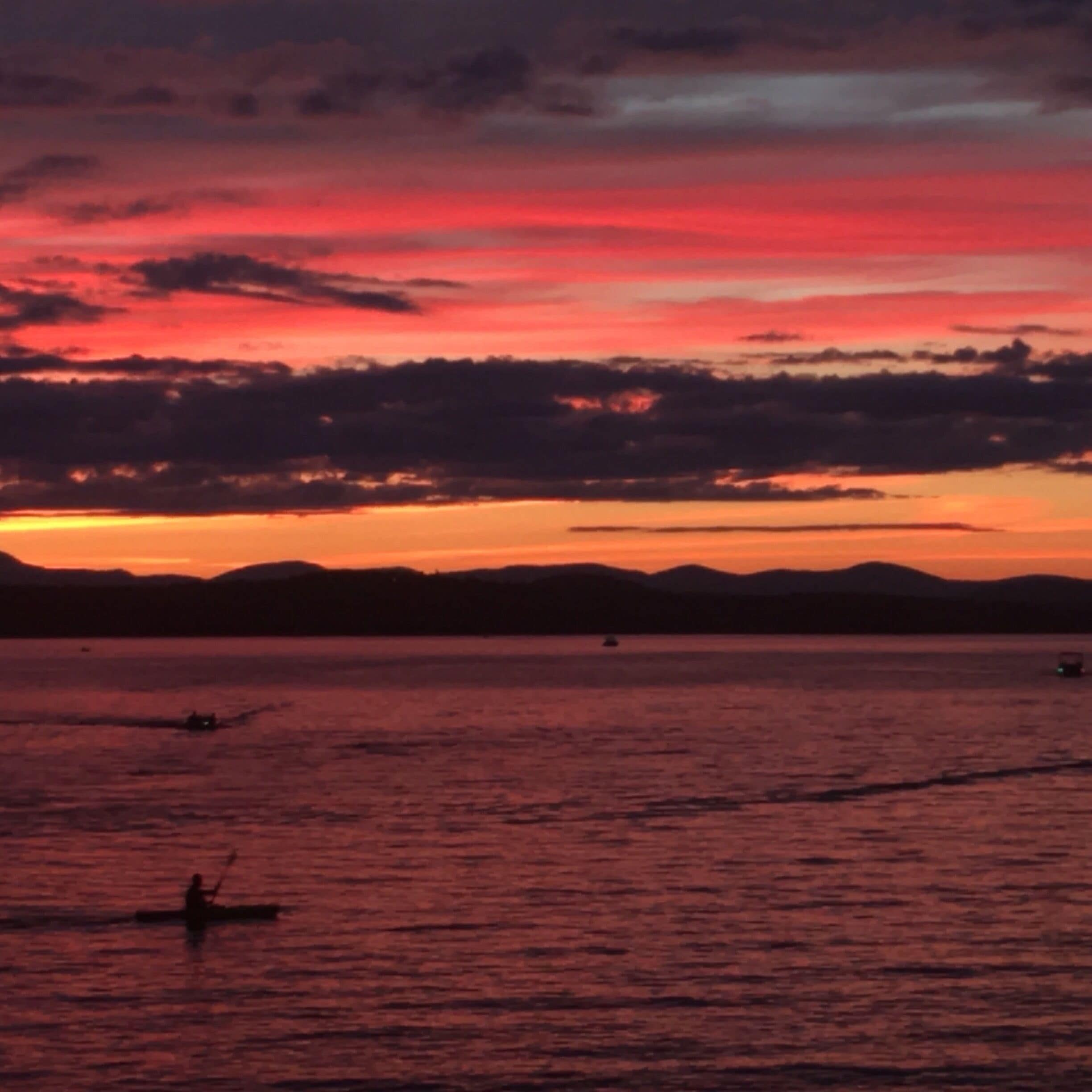 A sunset over a calm body of water with a silhouette of a person rowing a boat.