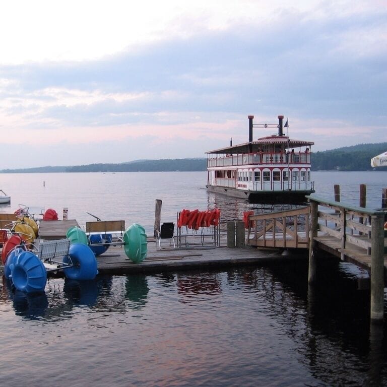 A paddle steamer docked at a pier with a wooden walkway and colorful life rings.