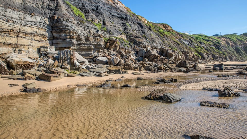 A rocky shoreline with layered cliffs and a clear, shallow water body.